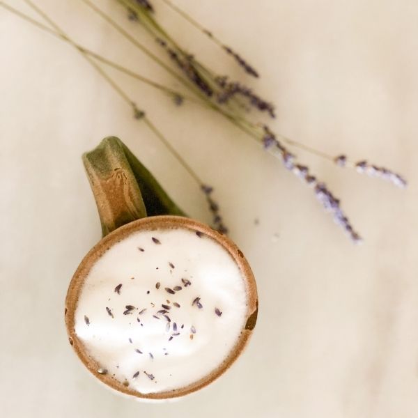 Lavender milk tea with lavender garnish brown potter handle and cup lip dried lavender white background