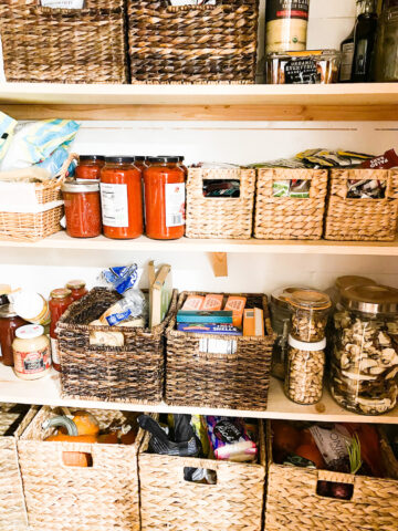 Pantry stocked with various items straw baskets for organization various glass jars filled with pantry items, pine board shelves.