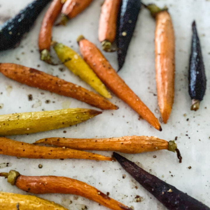 Orange purple and yellow roasted carrots on white parchment paper speckled with black pepper