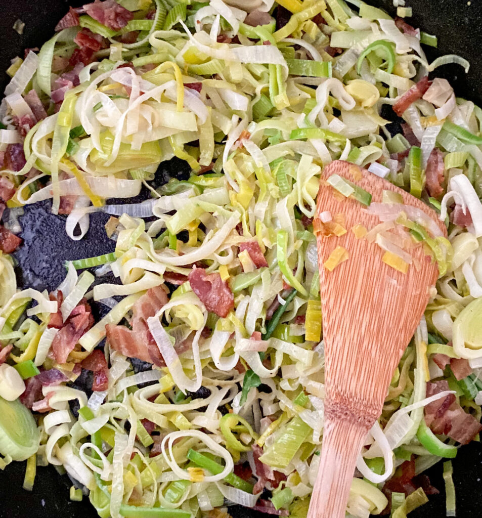 sautéed green white and yellow Leeks and pancetta in a cast iron pan wooden spatula