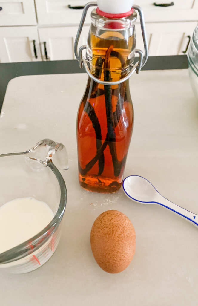 Vanilla in a clear glass bottle, measuring cup with milk egg and teaspoon. 