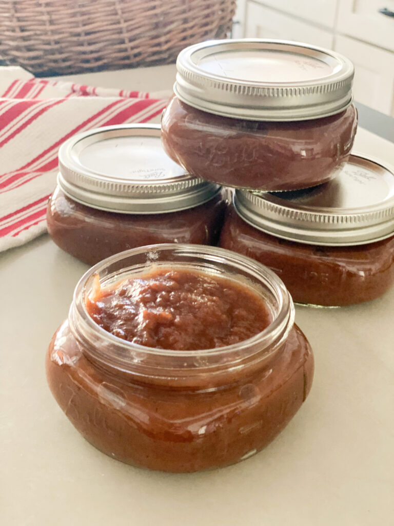 four ½ pint  jars of brown colored apple butter red and white towel in the background