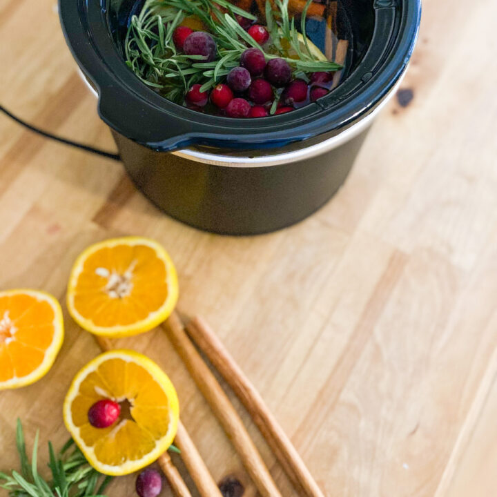 Overhead orange slices red cranberries whole cinnamon sticks rosemary, black mini crockpot with rosemary clove cranberries orange slices and cinnamon sticks filled with water