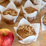 several golden brown sourdough cinnamon apple muffins apple in the forefront, butcher block countertop
