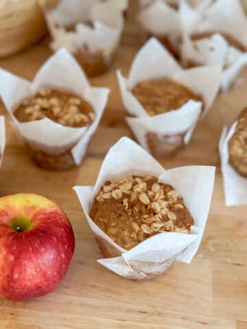 several golden brown sourdough cinnamon apple muffins apple in the forefront, butcher block countertop