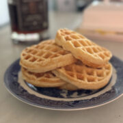 stack of four sourdough discard waffles on a blue and white plate, maple syrup and butter in the background
